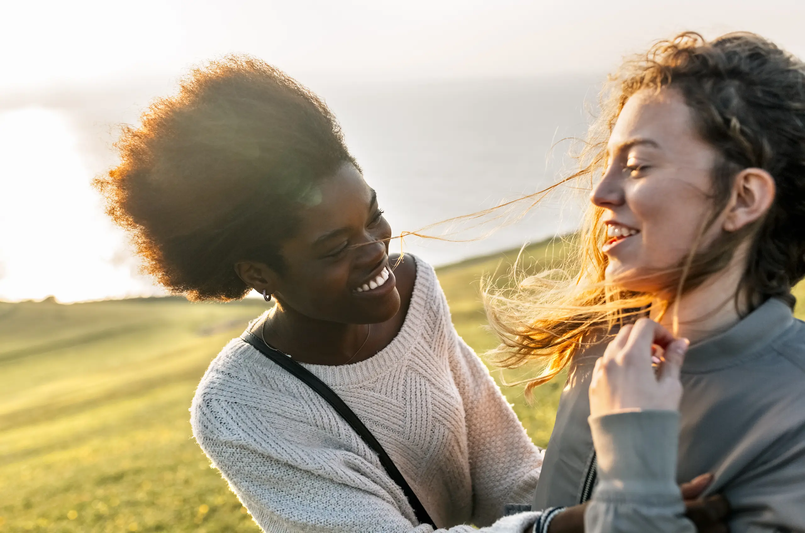 Einem Bild von zwei jungen Mädchen, die einander auf einem offenen Feld zulächeln.