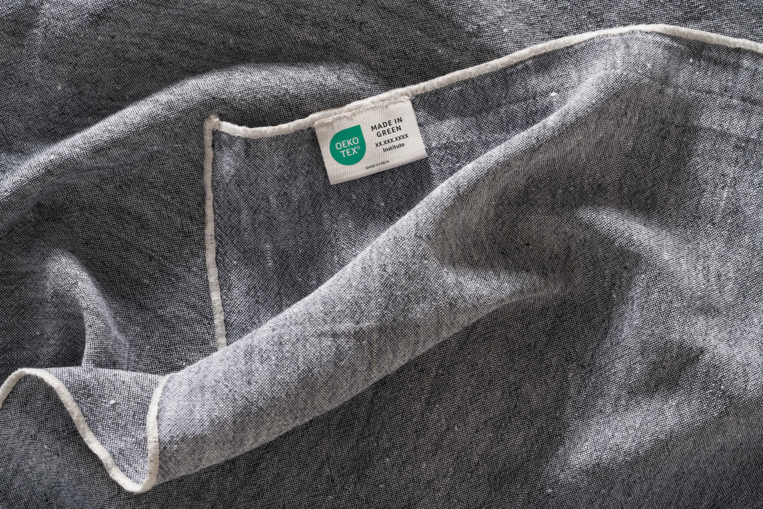 Abbildung eines grauen Textils mit OEKO-TEX® Etikett und Anhänger.