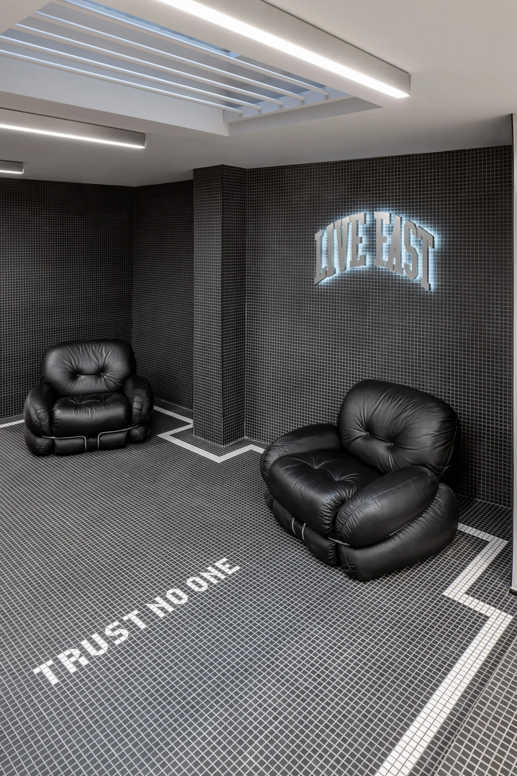 Zwei Oversize-Sessel im Umkleidebereich auf einem im Boden eingelassenen Schriftzug „Trust no one“