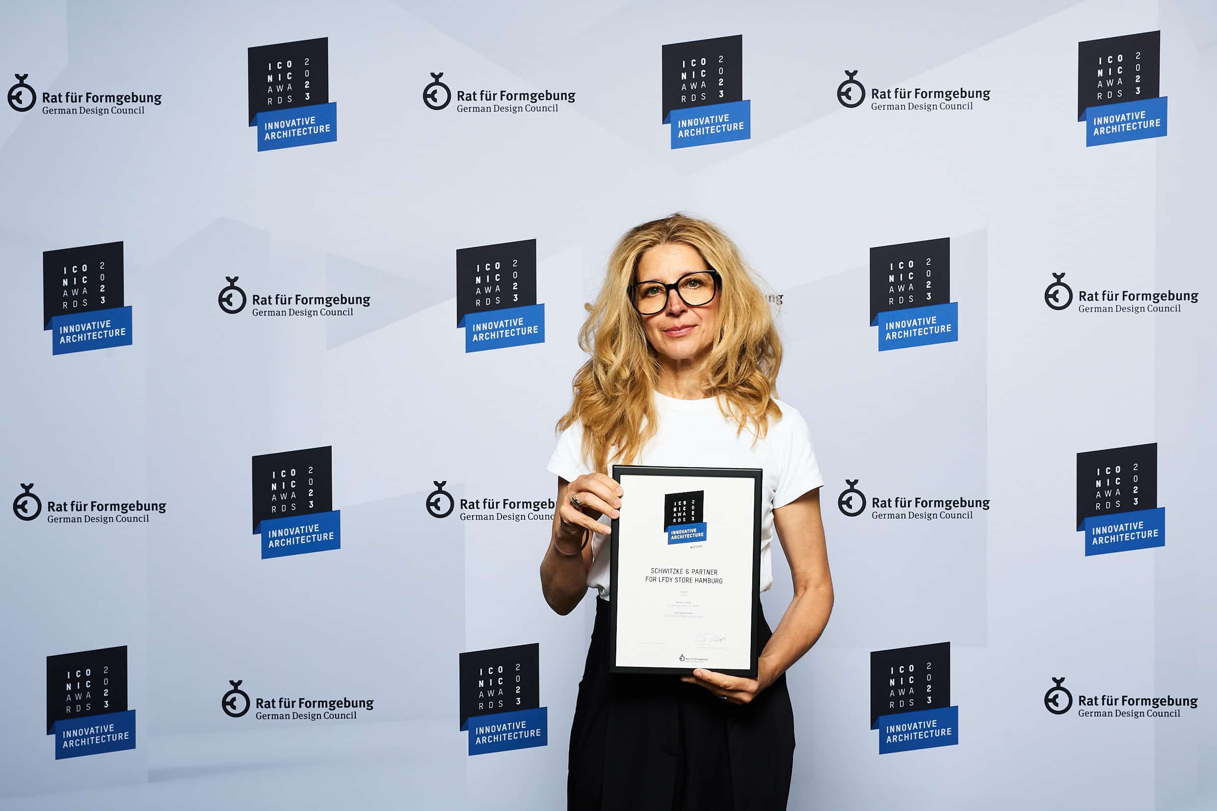 Tina Jokisch Geschäftsführerin mit Auszeichnung ICONIC AWARD vor blauer Wand