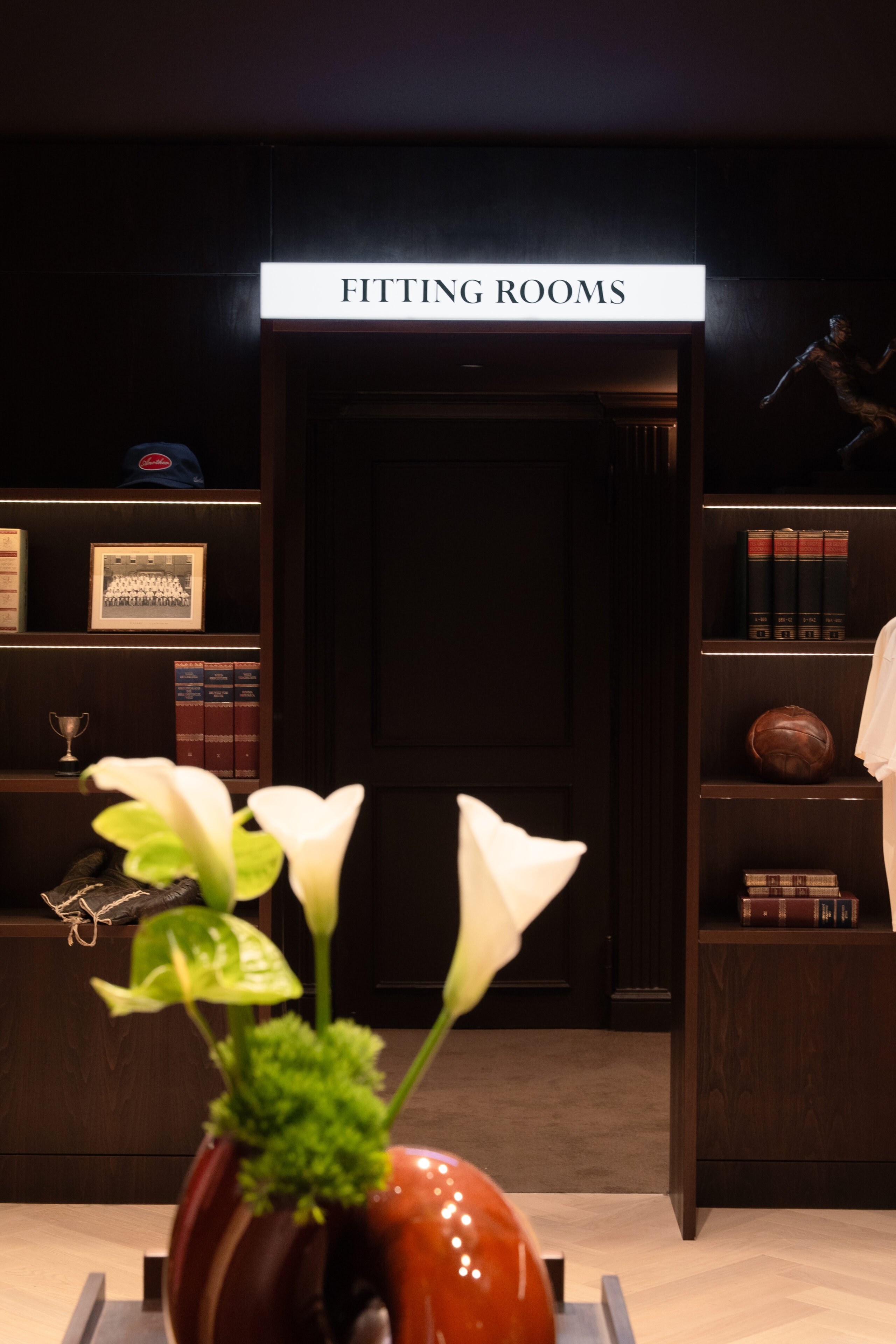 Modeladen mit sehr dunklem Holz, erinnert an eine Bibliothek. Die Leuchtschrift Fitting Room lädt in die Umkleidekabine ein.